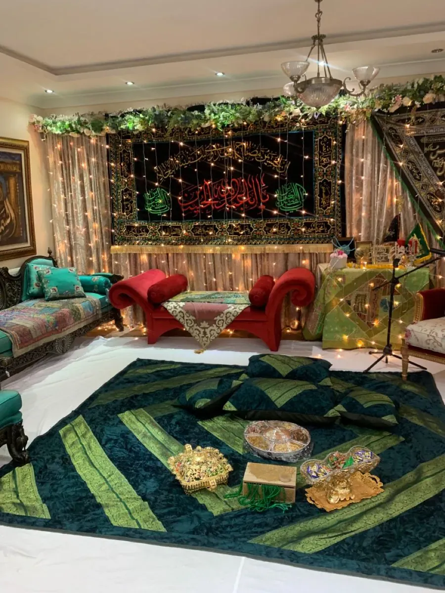 Mehfil-e-milad at home with an embroidered calligraphy banner, a red velvet bench and a green and gold floor spread