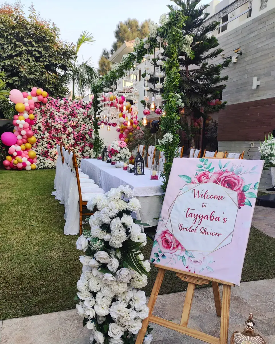 Bridal shower garden table with white flower arrangements, a pink and gold balloon garland and a floral sign