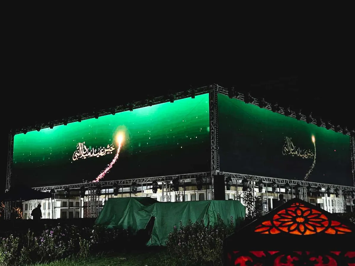 Wide night view of green LED screens on a truss showing a calligraphy greeting and a firework animation