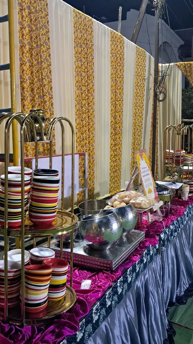 Catering counter with stacked colourful bowls on gold stands and hammered steel serving dishes — Baraka Events, Lahore