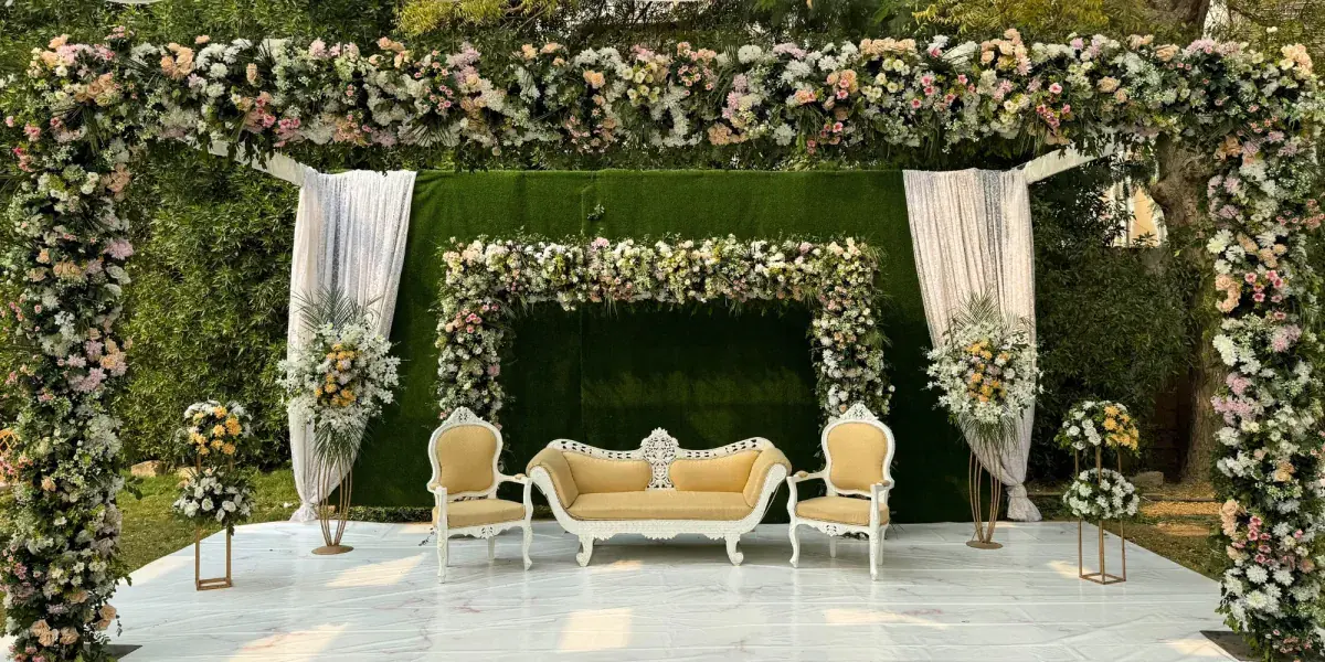 Garden-style floral arch frame over a cream sofa and two armchairs in front of a green hedge on a marble floor