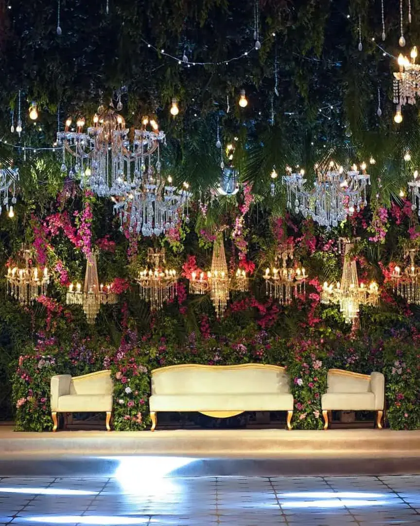 Baraat stage backdrop of hanging greenery, chandeliers and bougainvillea behind a cream sofa — Baraka Events, Lahore