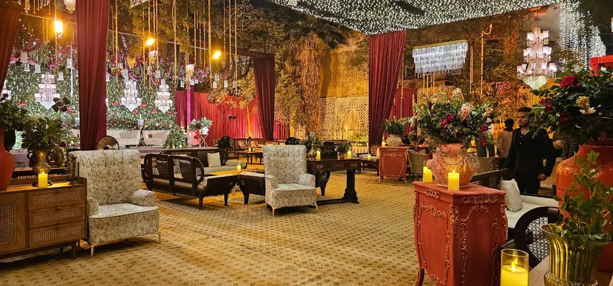 Baraat lounge of armchairs, wooden tables and candles facing a stage framed by red velvet drapes
