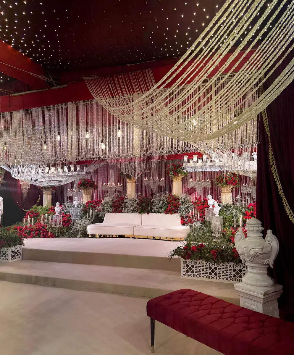 Baraat stage with curtains of hanging crystal strands, red roses, white urns and a white sofa