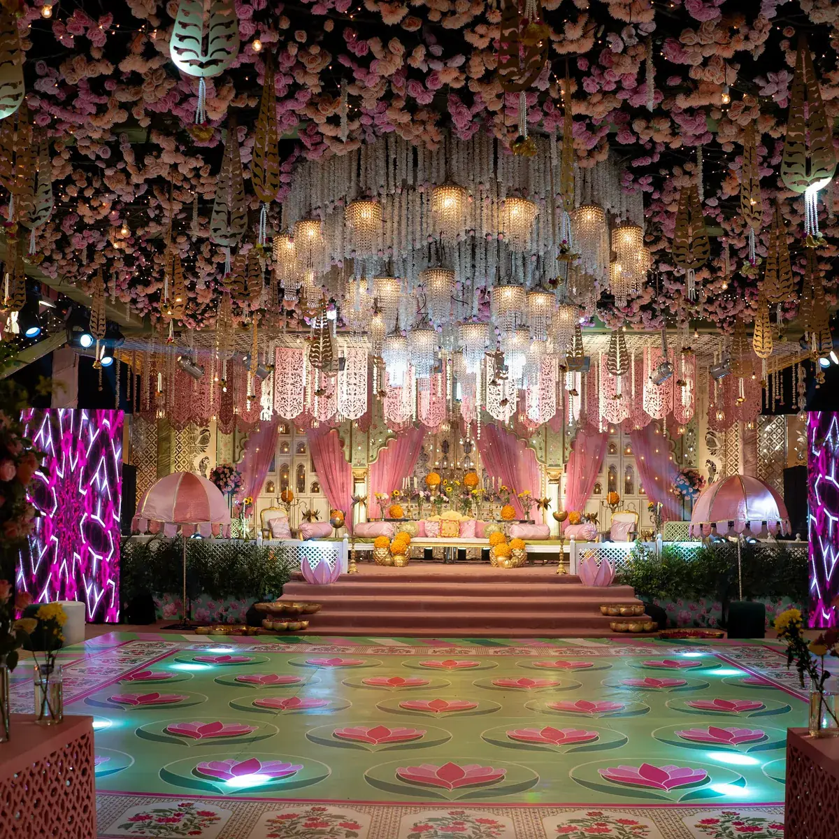 Stage under a ceiling of blush flowers and hanging crystal garlands with a lotus-pattern lit floor