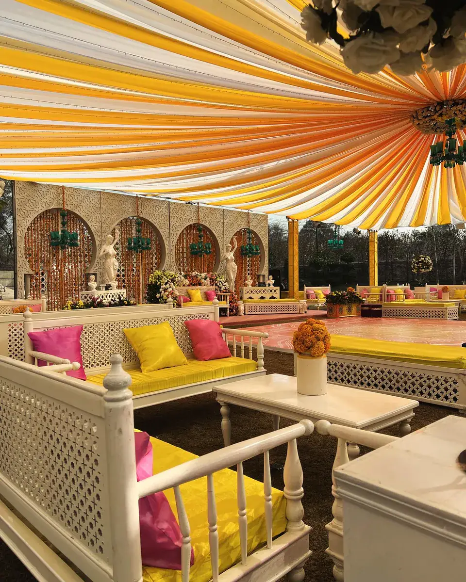 Mehndi seating of white lattice sofas with yellow and pink cushions under a draped canopy — Baraka Events, Lahore
