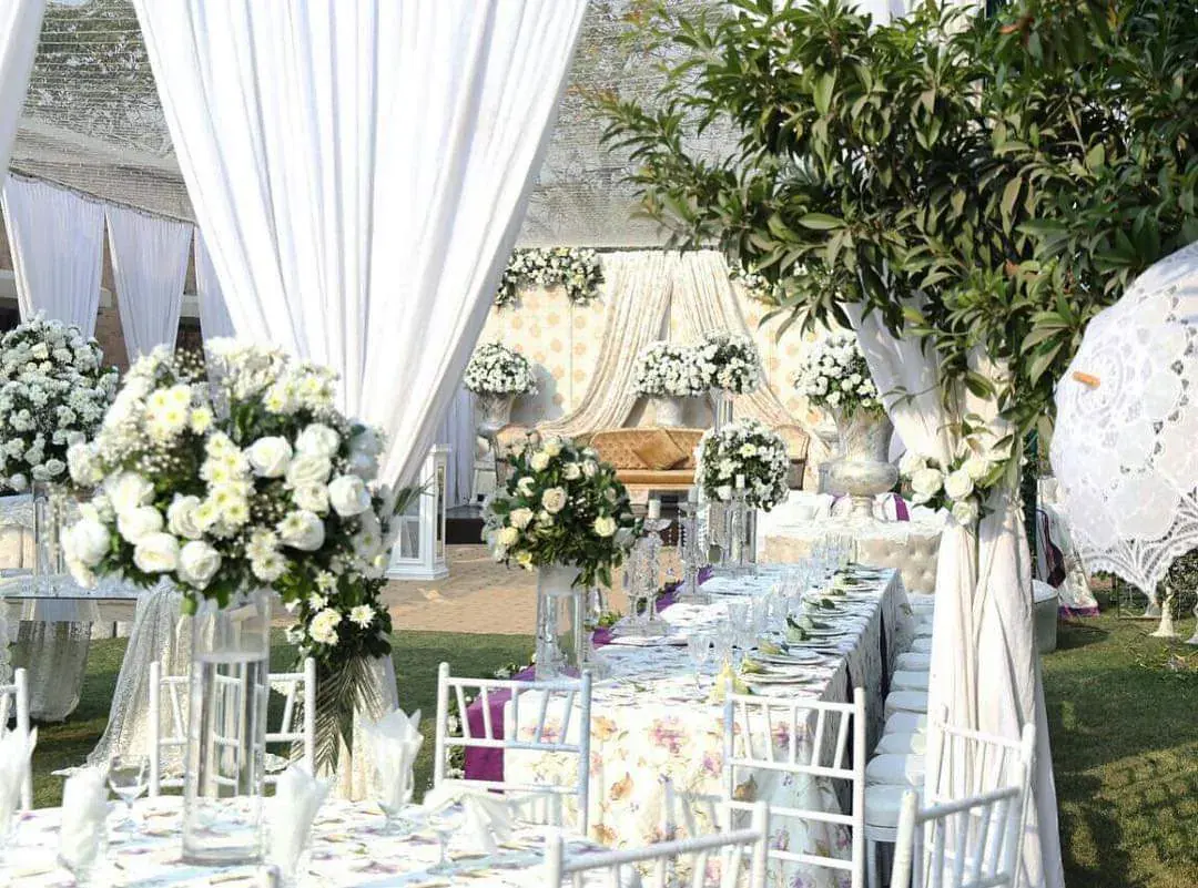 Garden walima banquet table with white floral centrepieces and white chairs under a draped white canopy