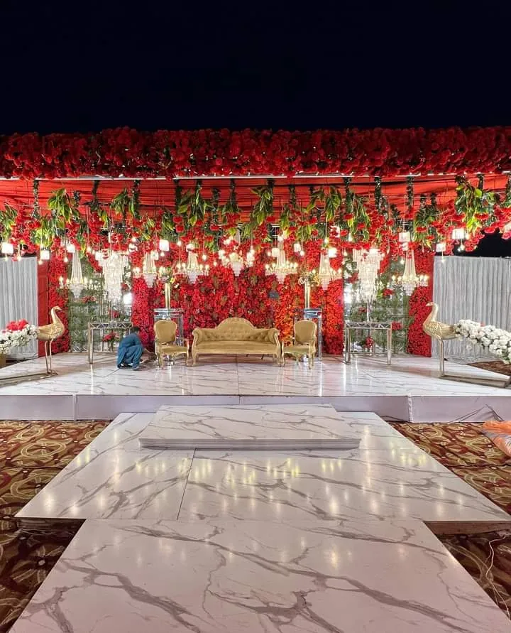 Baraat stage with a gold sofa against a wall of red flowers, hanging chandeliers and golden bird sculptures