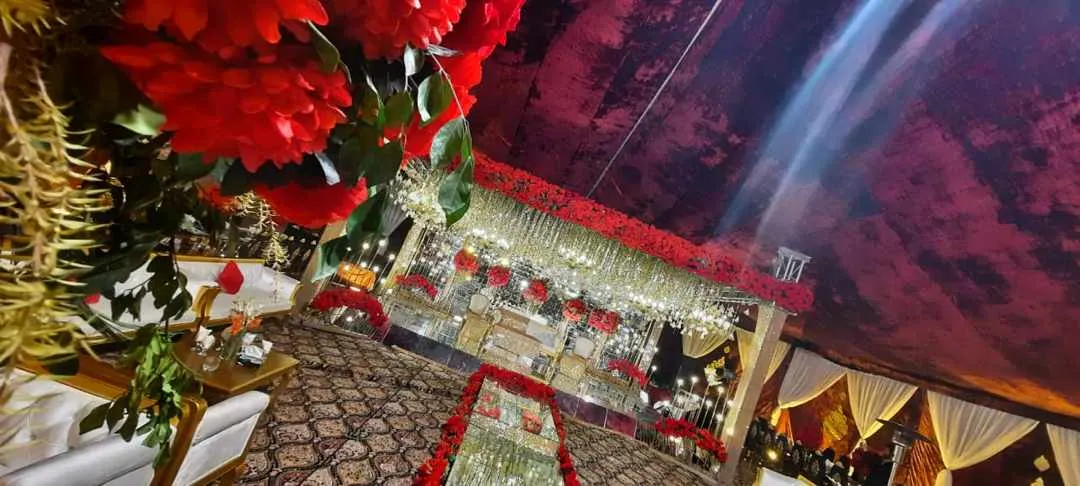 Red-petal-lined walkway to a baraat stage under a ceiling of hanging beads, photographed at night