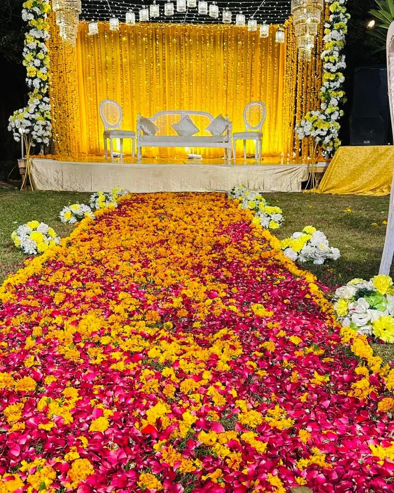 Mehndi aisle of marigold and pink rose petals leading to a yellow-draped stage with a white sofa — Baraka Events, Lahore