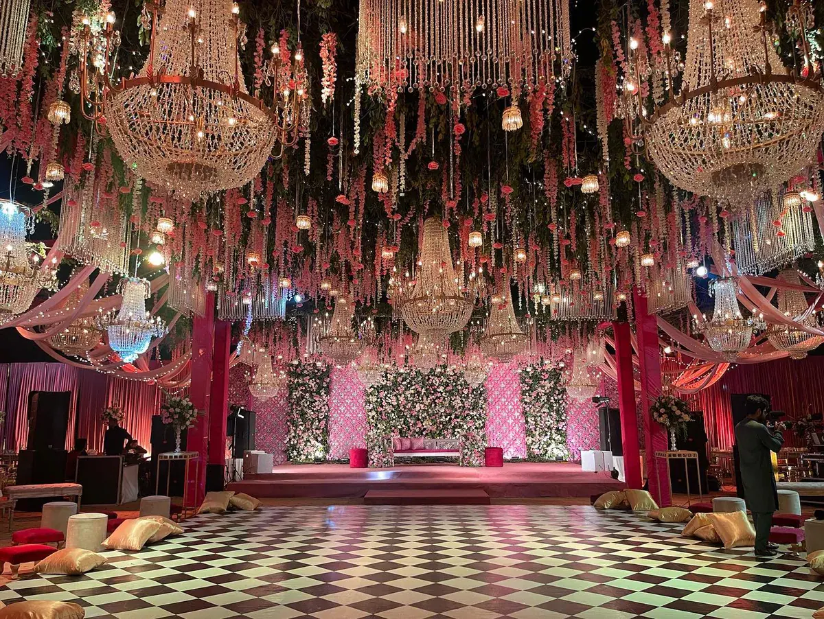 Mehndi stage and checkerboard dance floor under hanging chandeliers and pink flower garlands