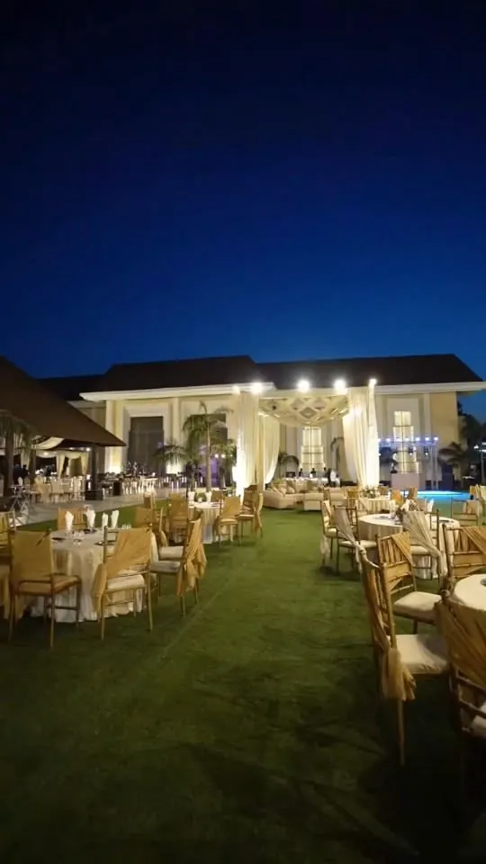 Farmhouse wedding lawn at night, with chair-covered tables and a white-draped entrance beside a lit house