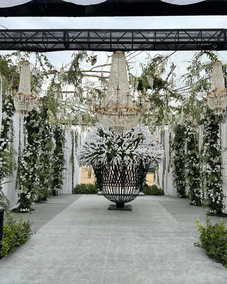Garden walkway for a walima with a large black metal basket of white flowers and hanging chandeliers
