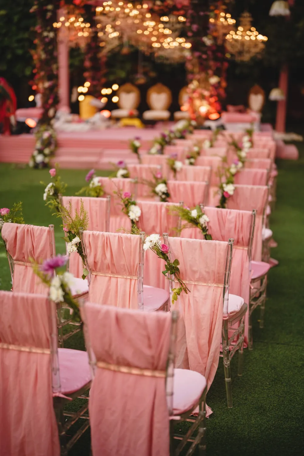 Blush chiffon-draped aisle chairs leading to a candlelit floral wedding stage