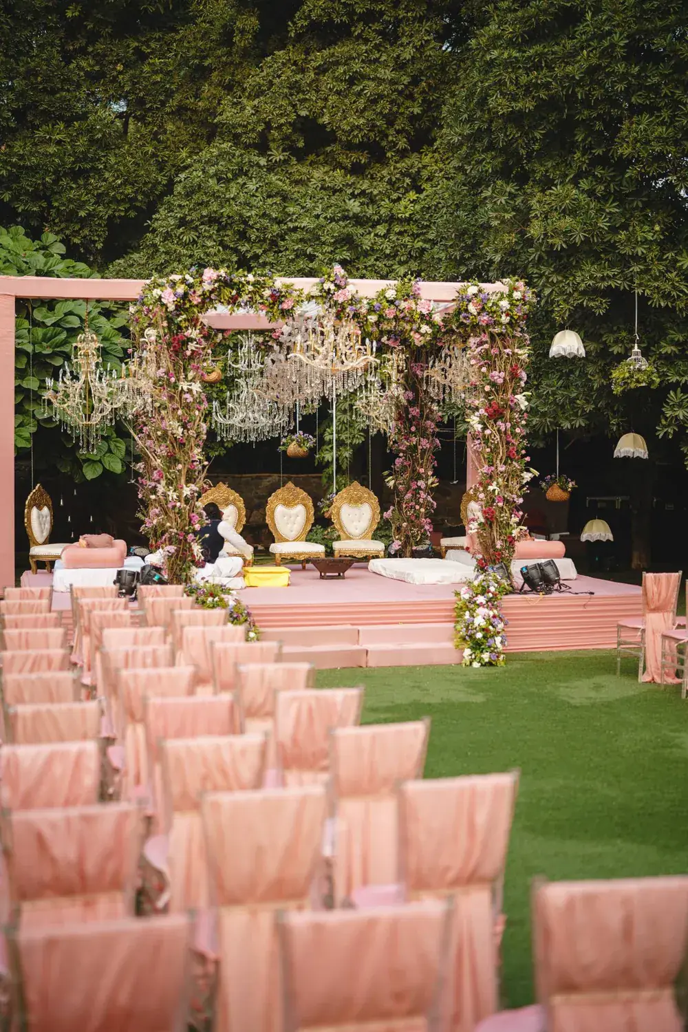 Floral wedding arch with hanging crystal chandeliers over gold ceremony chairs