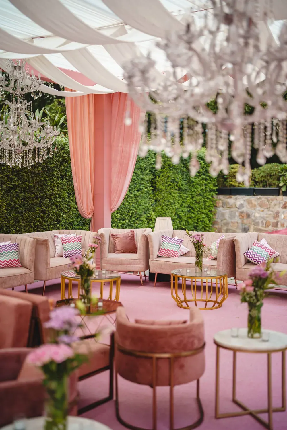 Blush lounge seating with crystal chandeliers under a draped canopy at an outdoor reception